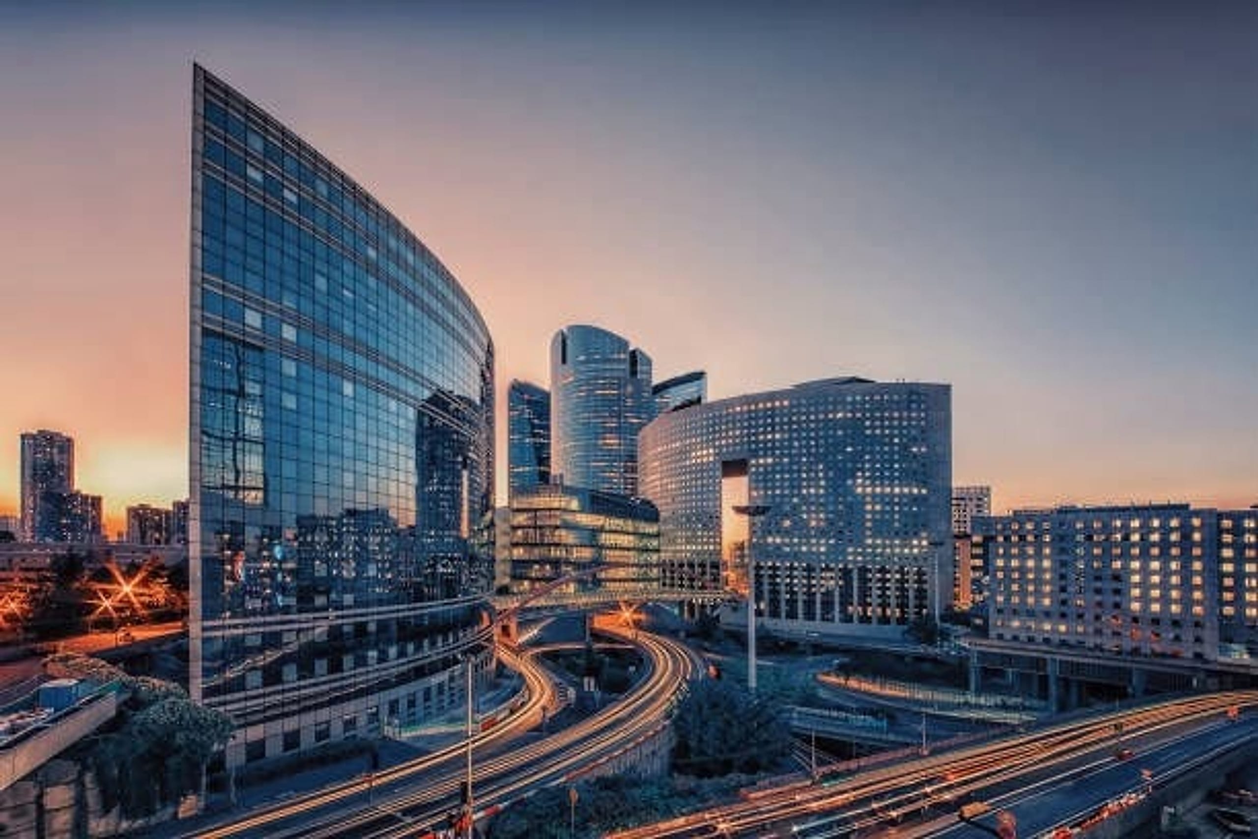 Modern commercial glass high-rise towers and illuminated highway at dusk