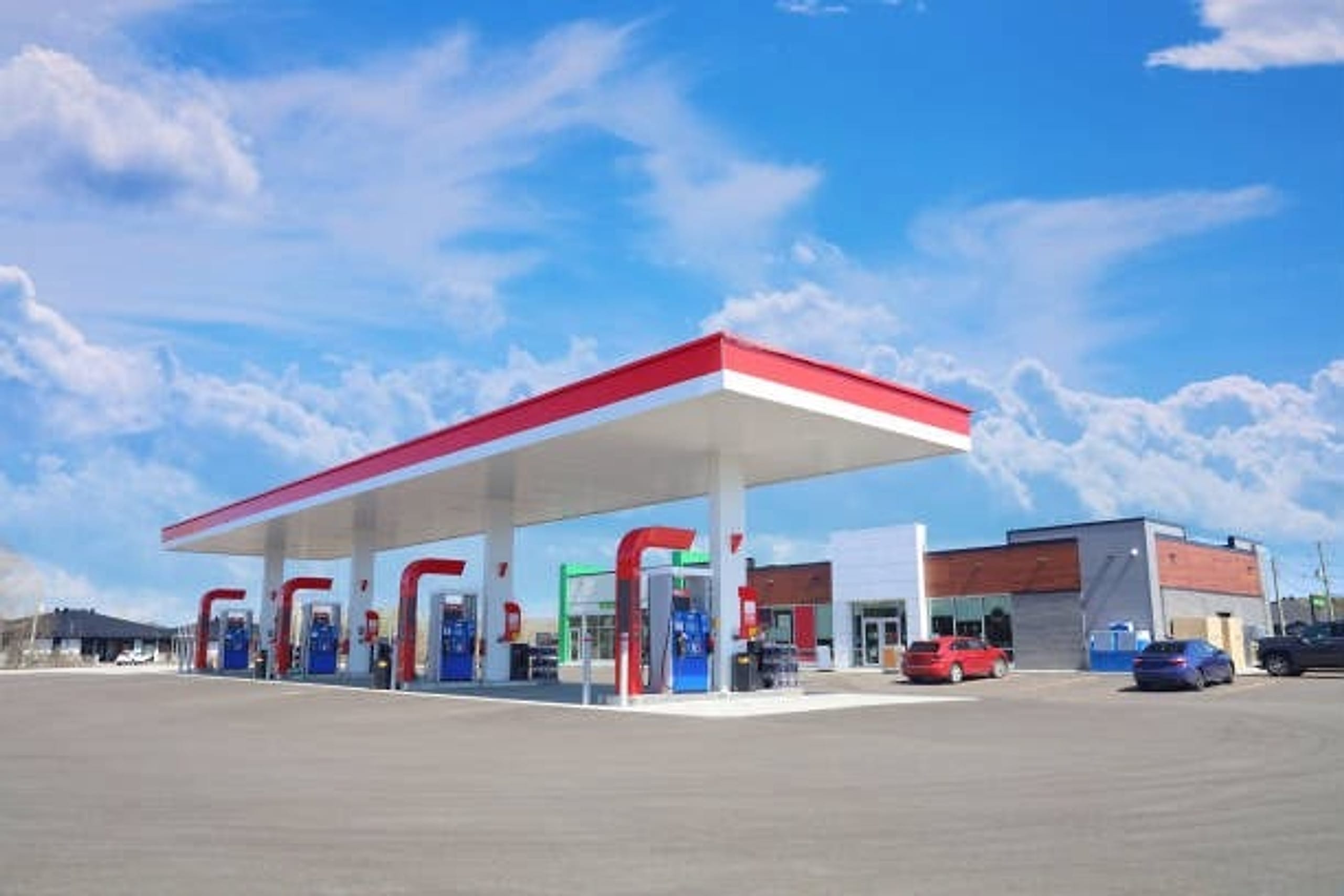 Modern commercial gas station with red canopy and illuminated fuel bays under a clear blue sky